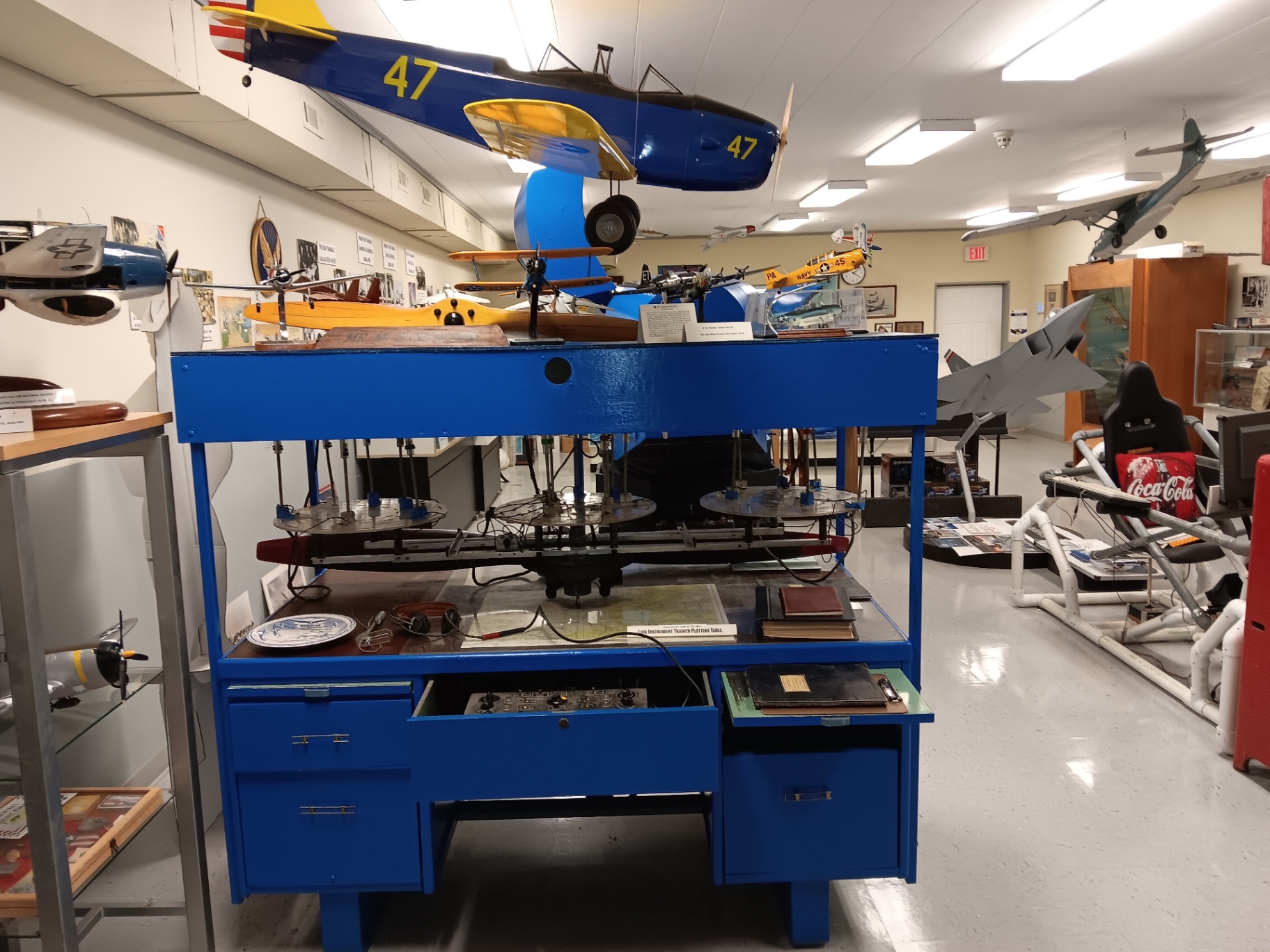The Link Instrument Trainer plotting table, opened up to show the linkage inside — with hand-built trainers and fighters hanging above it.