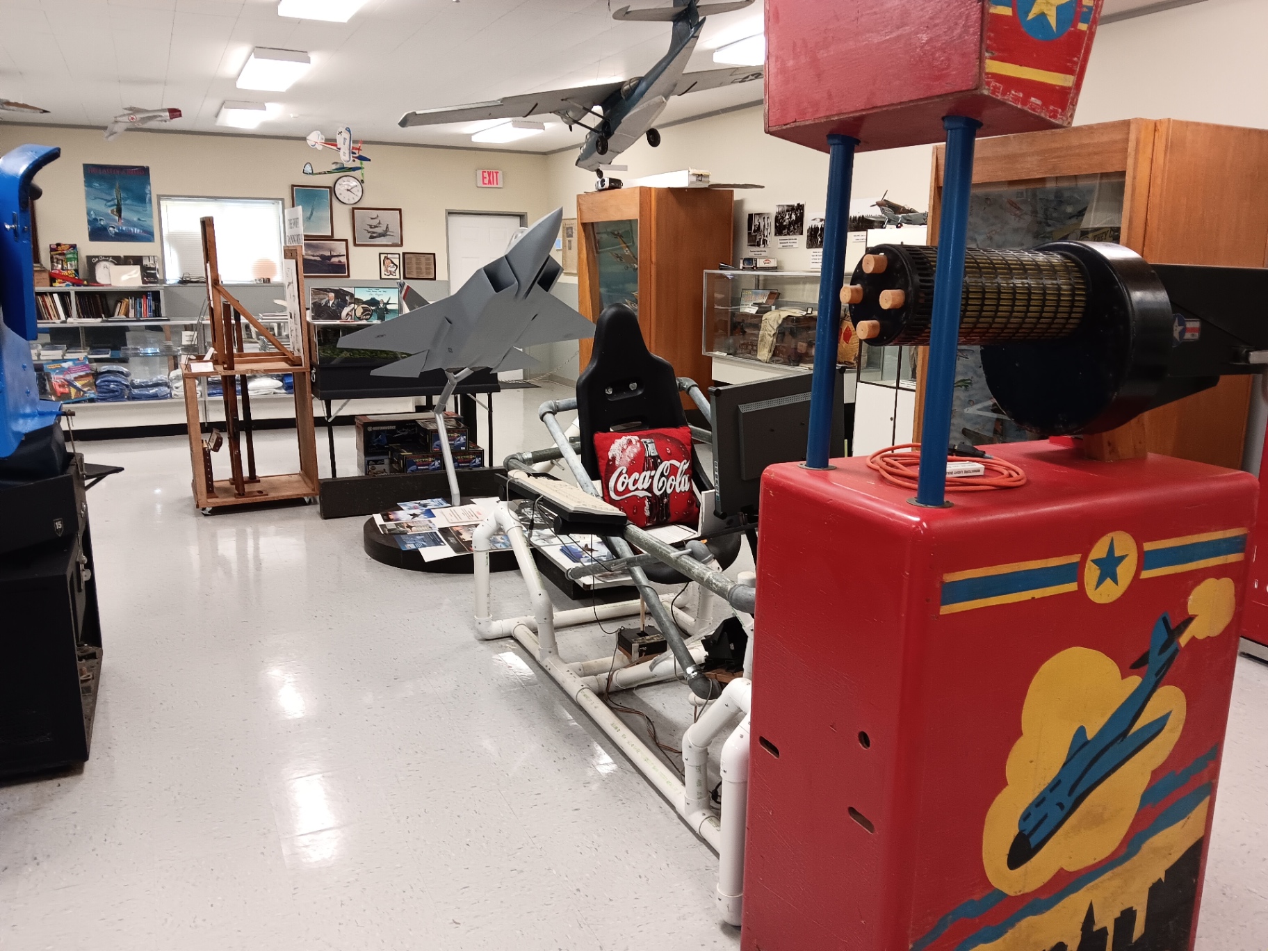The AeroBall SimCab rig where visitors fly, with the red Link trainer drum in the foreground and an F-22 model on the deck.