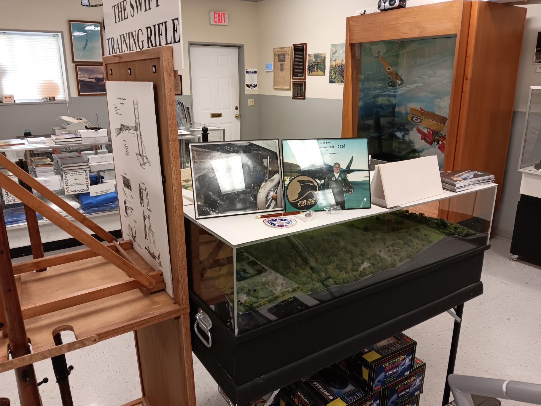 A signed F-22 Raptor print and a scale terrain diorama near the front counter, with a WWI dogfight display beyond.